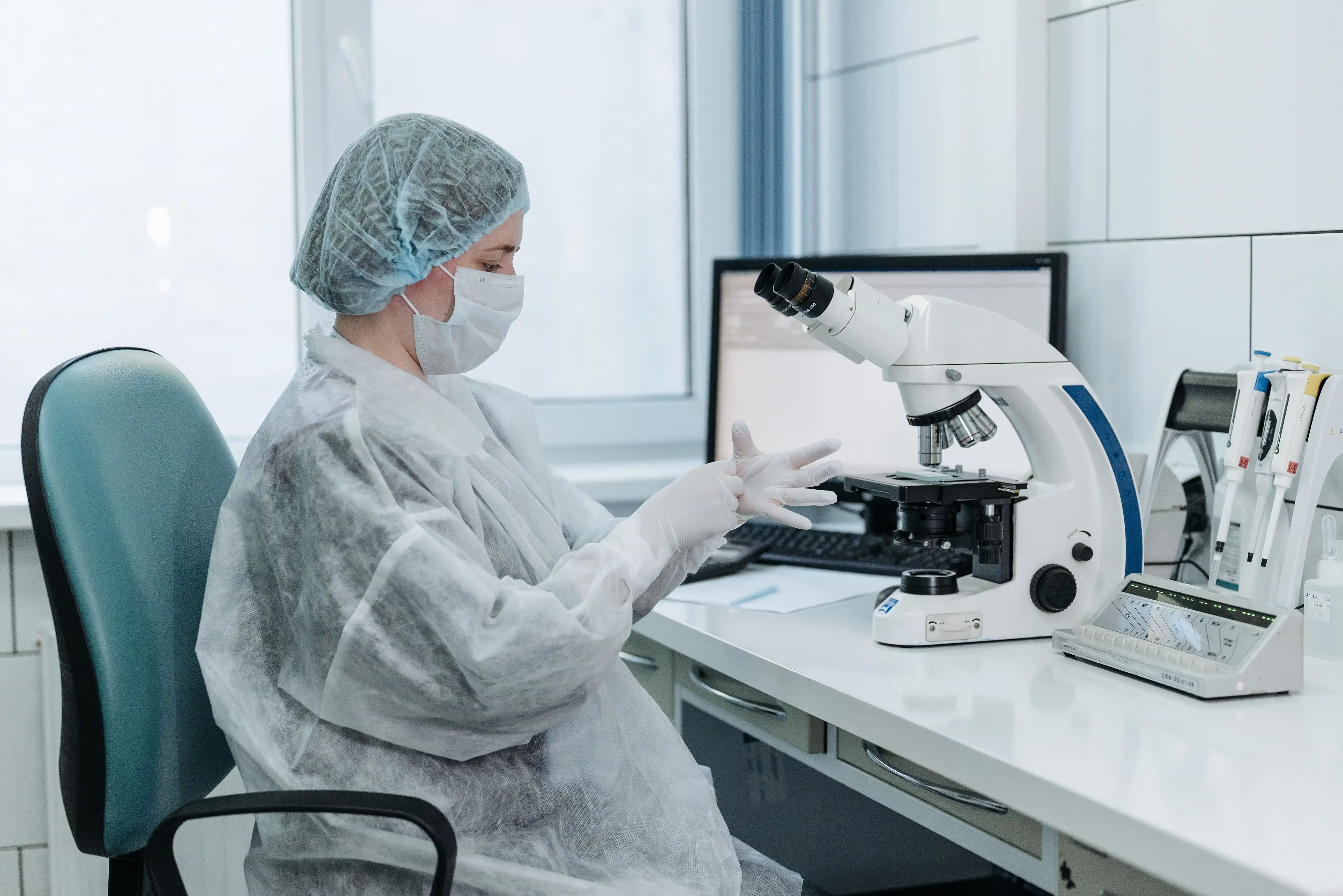 Technicienne de laboratoire en équipement de protection examinant des échantillons sous un microscope